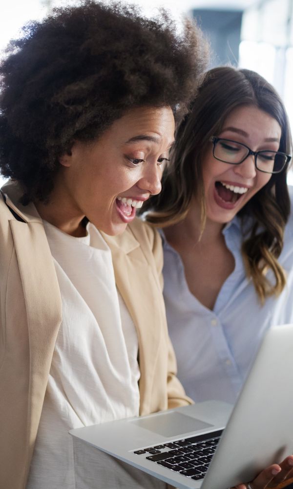 two women smiling and celebrating in front of a laptop